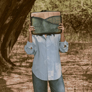 Person holding a green vegan leather bag over their face in a natural setting