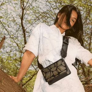 Woman in a white outfit holding a black handbag with leaf patterns outdoors.