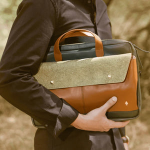 Person holding a brown and green vegan leather bag outdoors