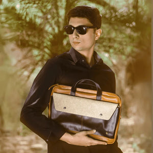 Man holding a brown vegan leather briefcase with a blurred natural background