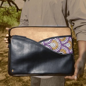Person holding a clutch bag with black vegan leather and beaded design in a natural setting