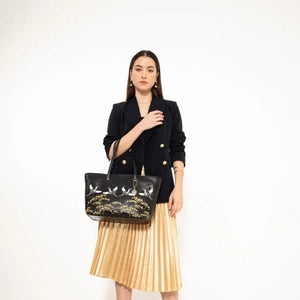 Woman holding a black handbag with gold accents against a white background