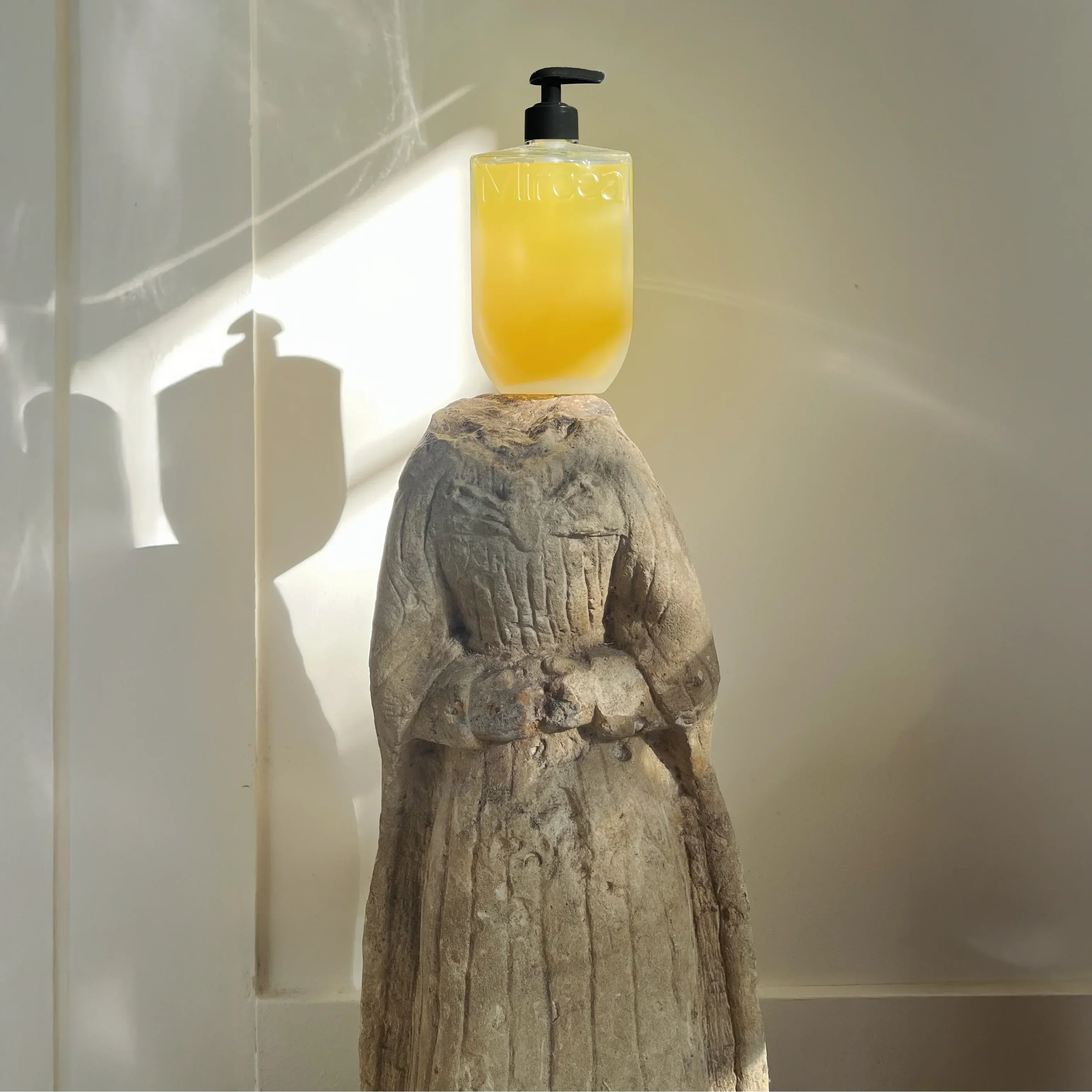 Yellow bottle with black pump on a stone sculpture against a light background