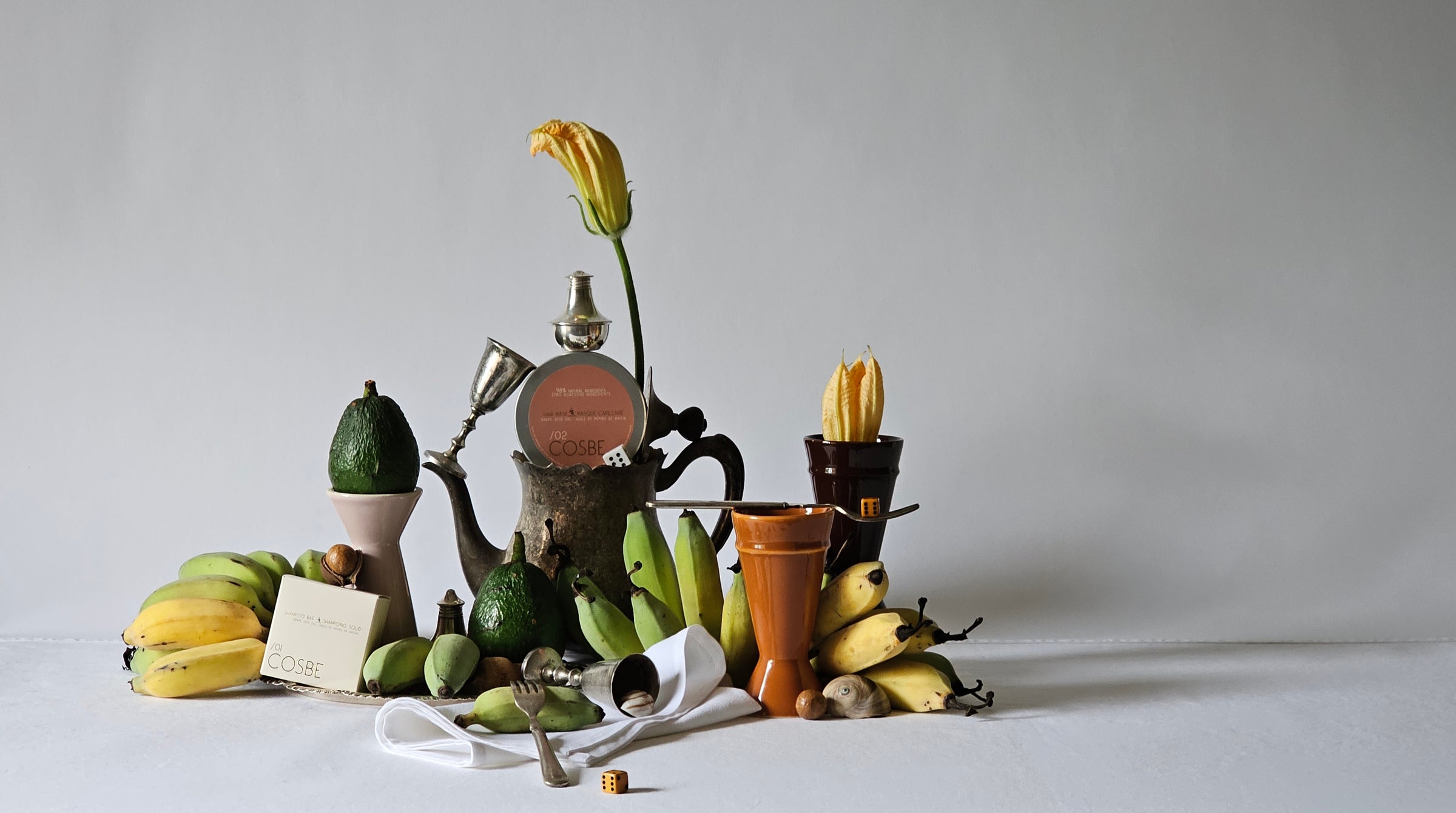 Still life arrangement with fruits, a teapot, and decorative items on a light surface showcasing a selection of Deed Industries Ethical Luxury Goods.