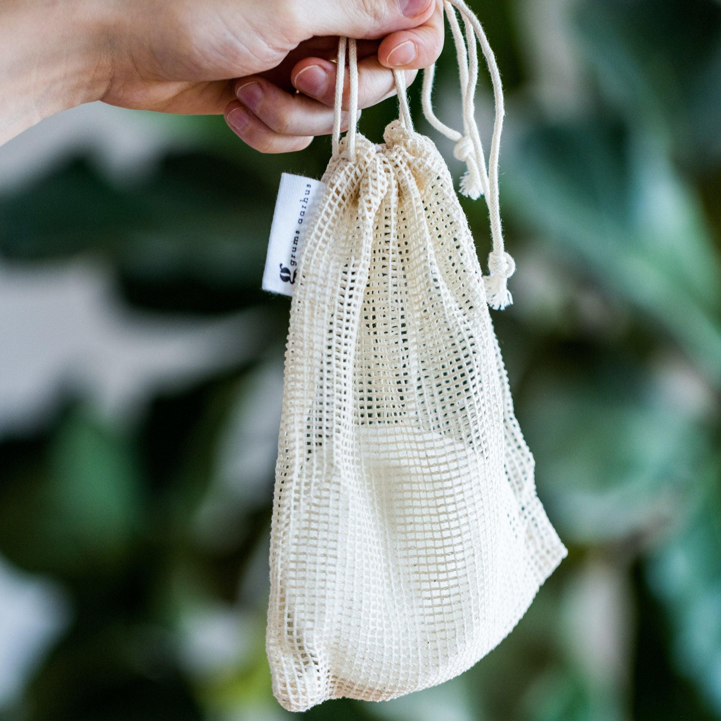 A hand holding a reusable bamboo cotton pad with a visible brand label, against a blurred greenery background.