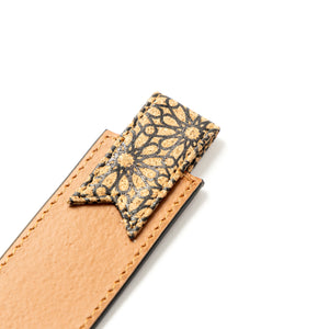 Close-up of a beige veagn leather strap with a decorative black and gold star-shaped clip on a white background