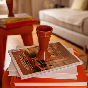 a sustainably made caramel mazagran coffee cup on a stack of magazines in a orange and  red toned living room.