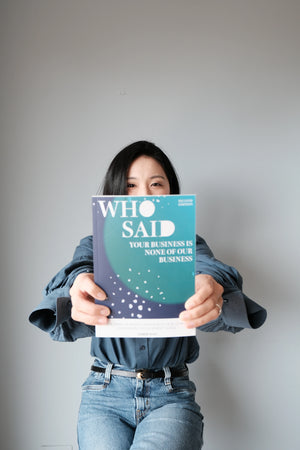Person holding a book titled 'WHO SAID YOUR BUSNESS IS NONE OF OUR BUSINESS' against a plain background