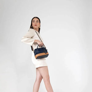 Woman holding a navy blue handbag with a brown strap against a white background