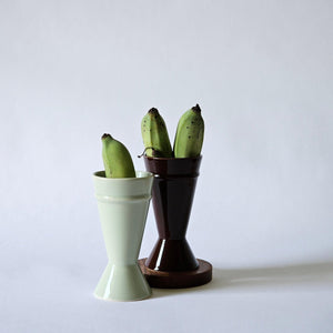Two mazagran coffee cups shown against a white background with small, green bananas