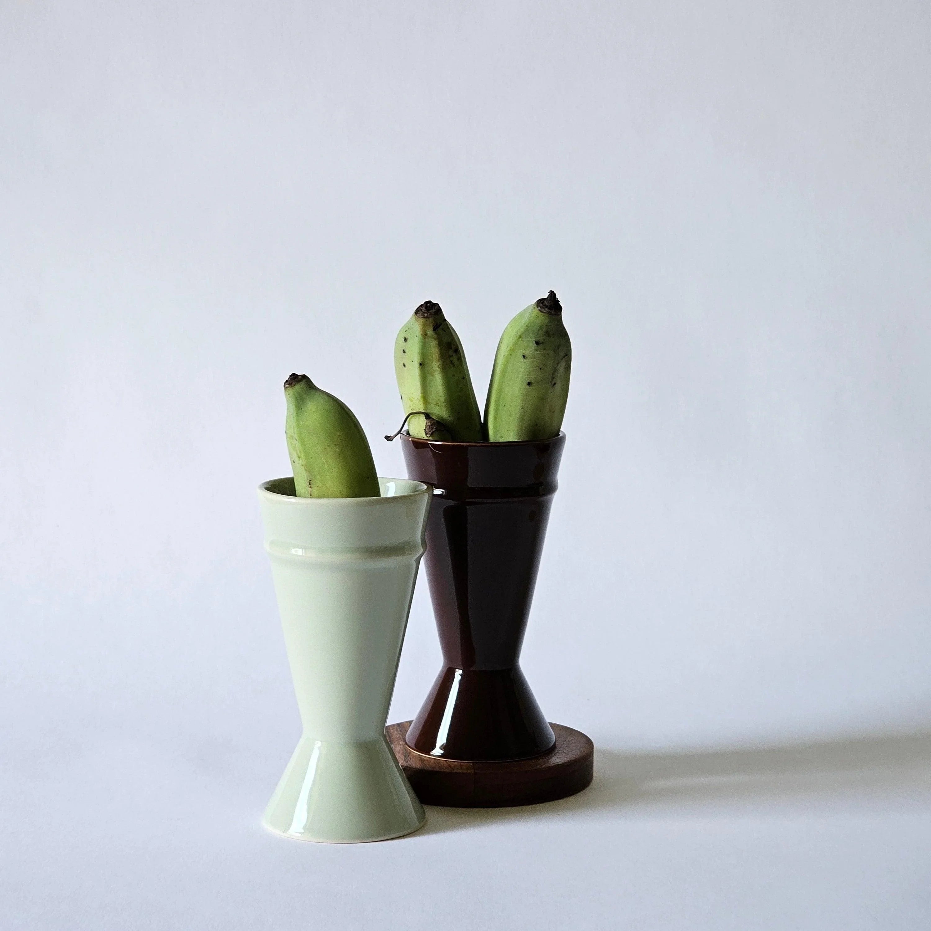 Two mazagran coffee cups shown against a white background with small, green bananas