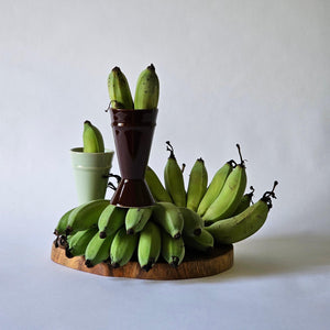 Mazagran coffee cups sitting in an arrangement of green, small bananas