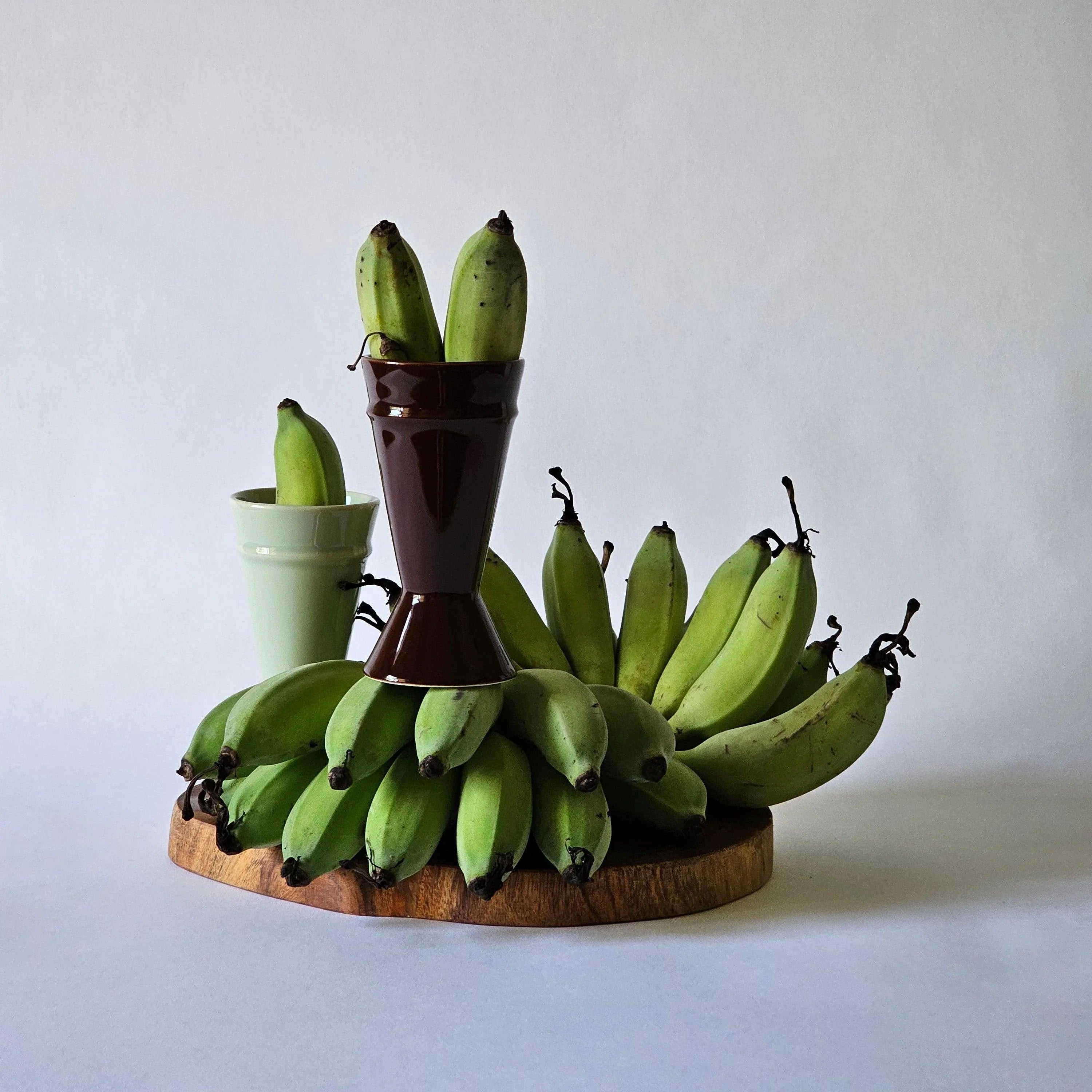 Mazagran coffee cups sitting in an arrangement of green, small bananas