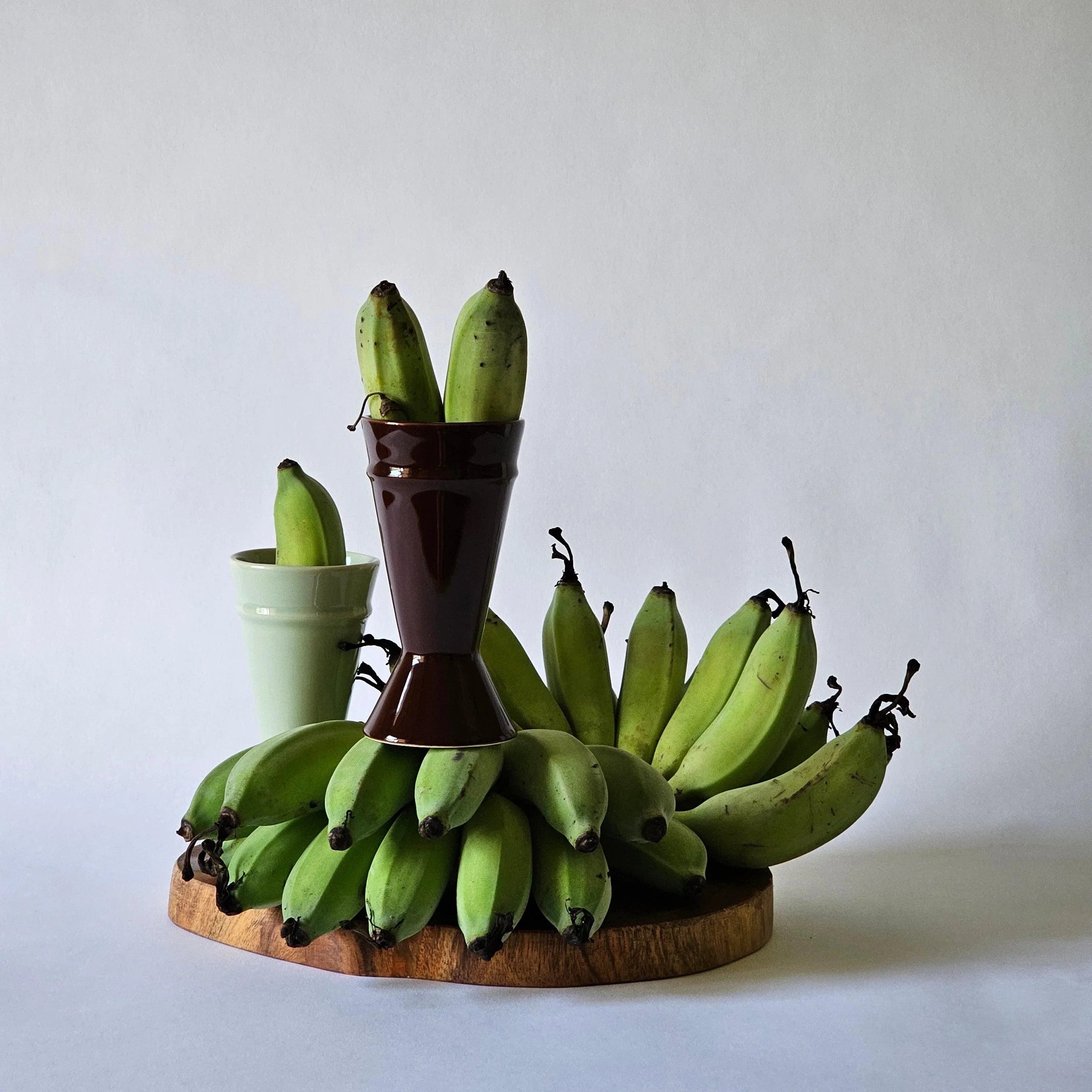 Sustainably produced mazagran coffee cups sitting on a dark board with green bananas
