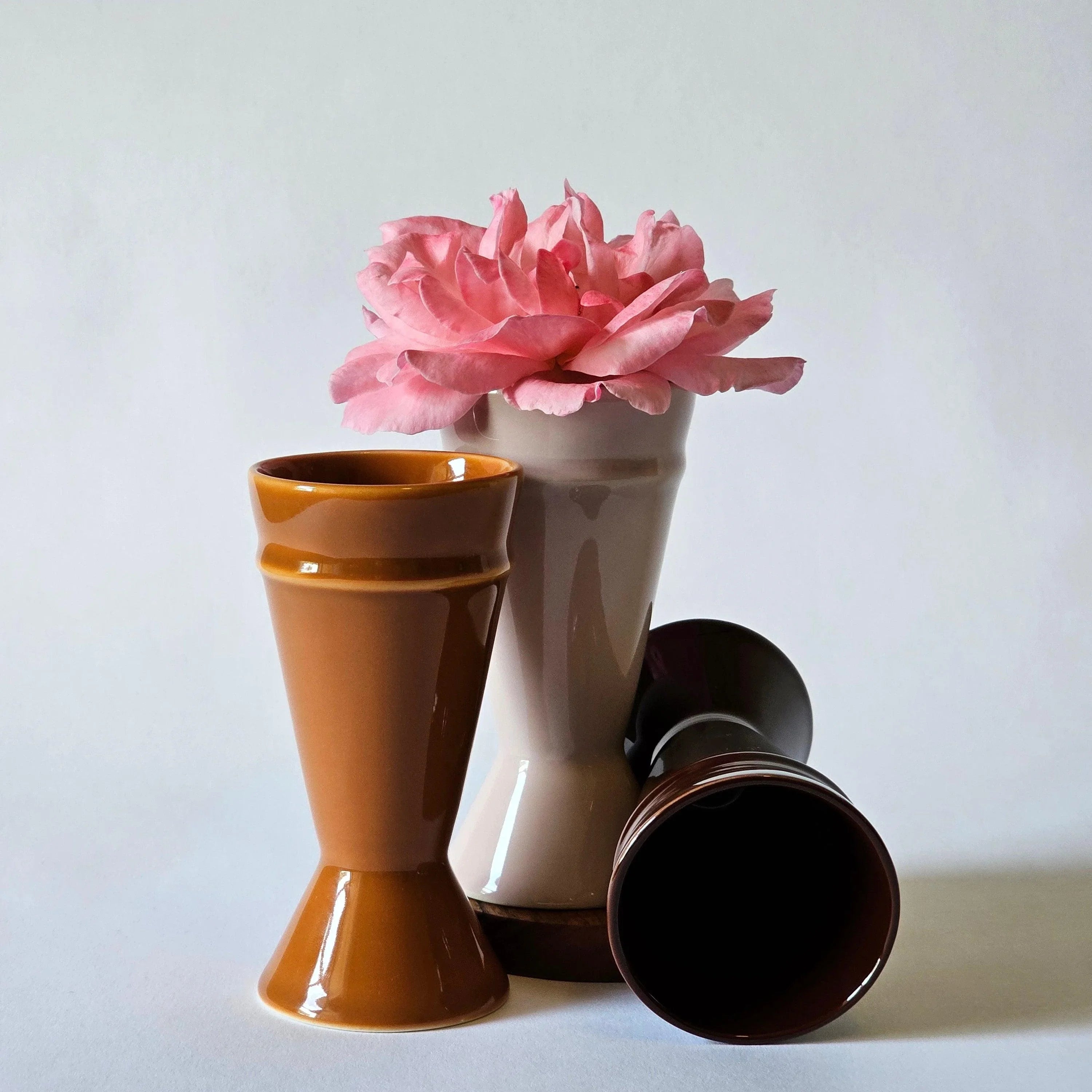 Caramel, Chocolate and blush pink Mazagran coffee cups arranged with a pink rose on a white background