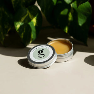 Two small cylindrical containers with black lids on a light surface with green leaves in the background
