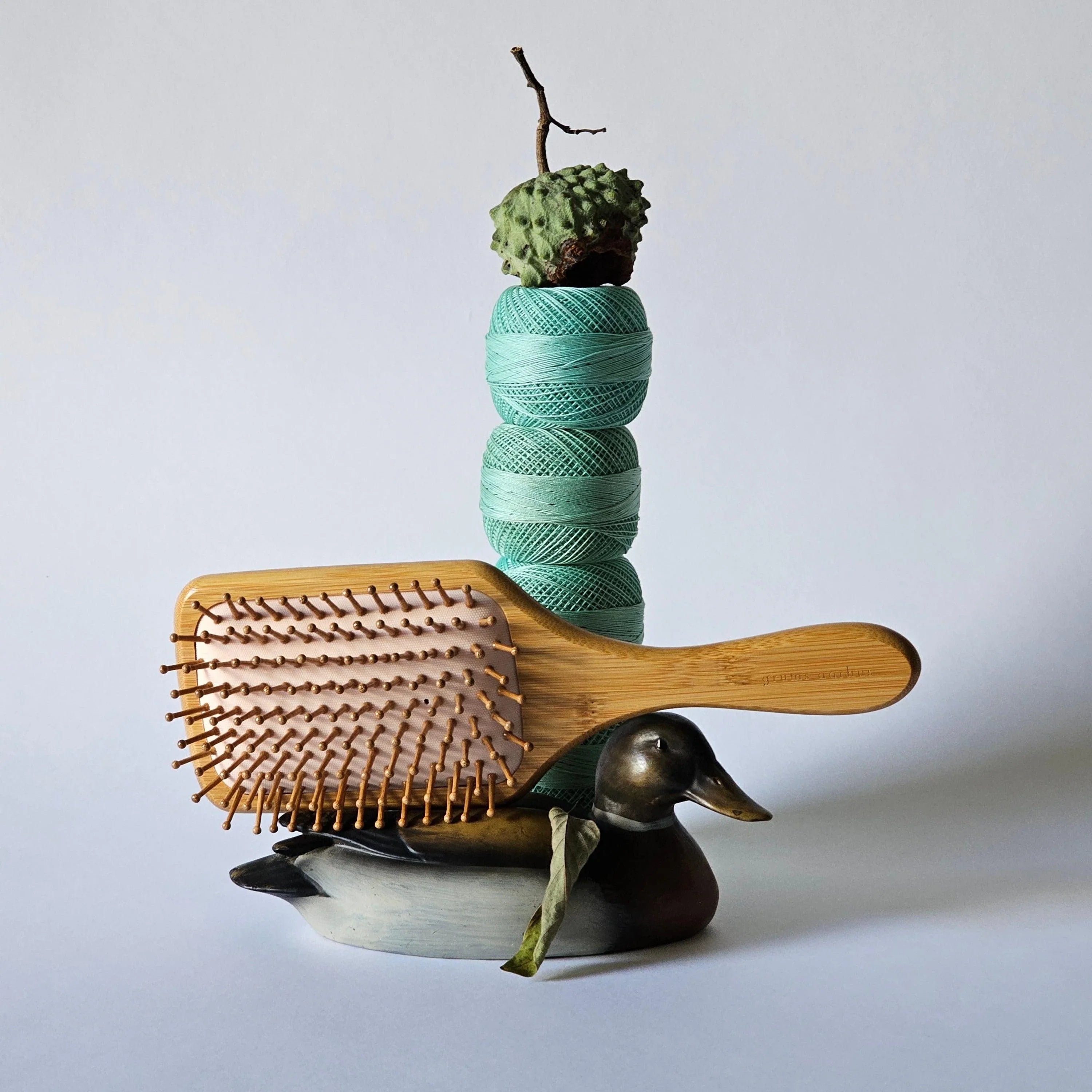 Wooden hairbrush, spool of green yarn, and decorative duck on a light gray background