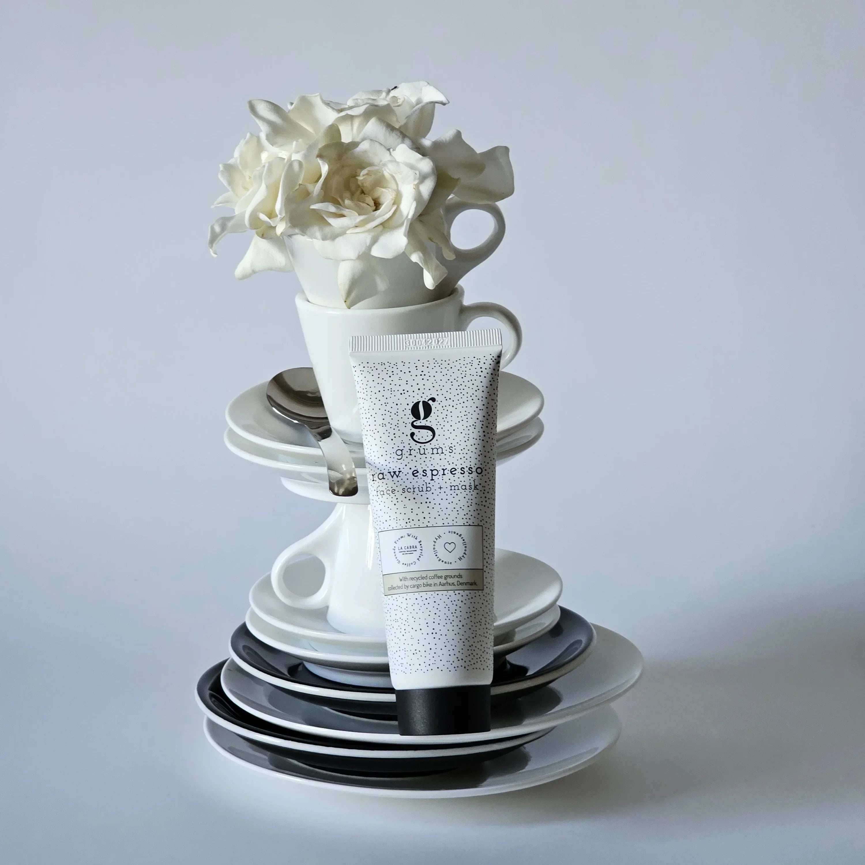 grums espresso face scrub and mask styled against a stack of cups and saucers with a large white rose