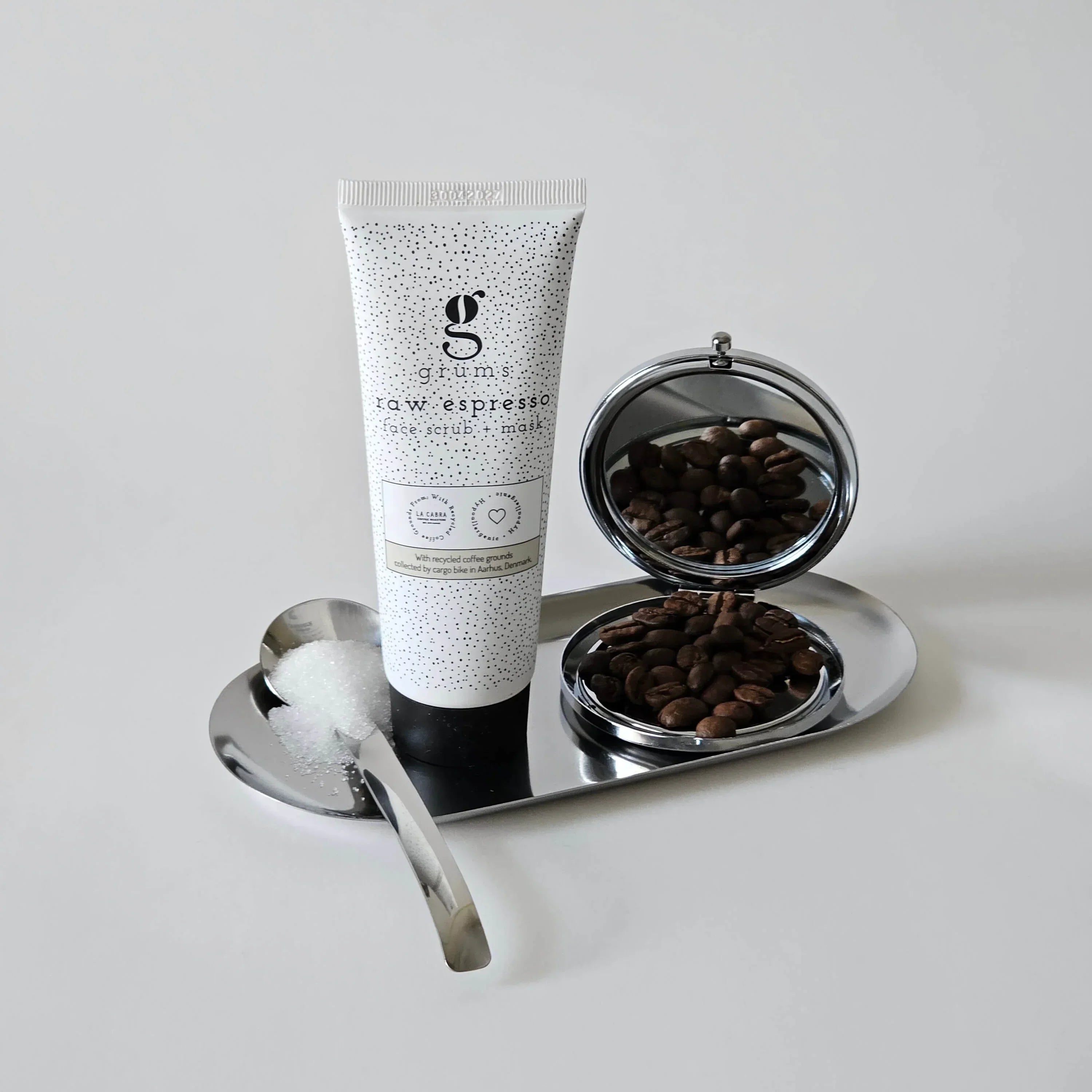 Tube of cream labeled grums espresso facial scrub & mask on a silver tray with coffee beans