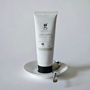 Tube of raw coffee hand scrub on a white plate with a white background