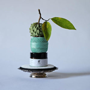 Green yarn ball with a branch and leaves on a gray background. hydra calm moisturizer sitting in the middle