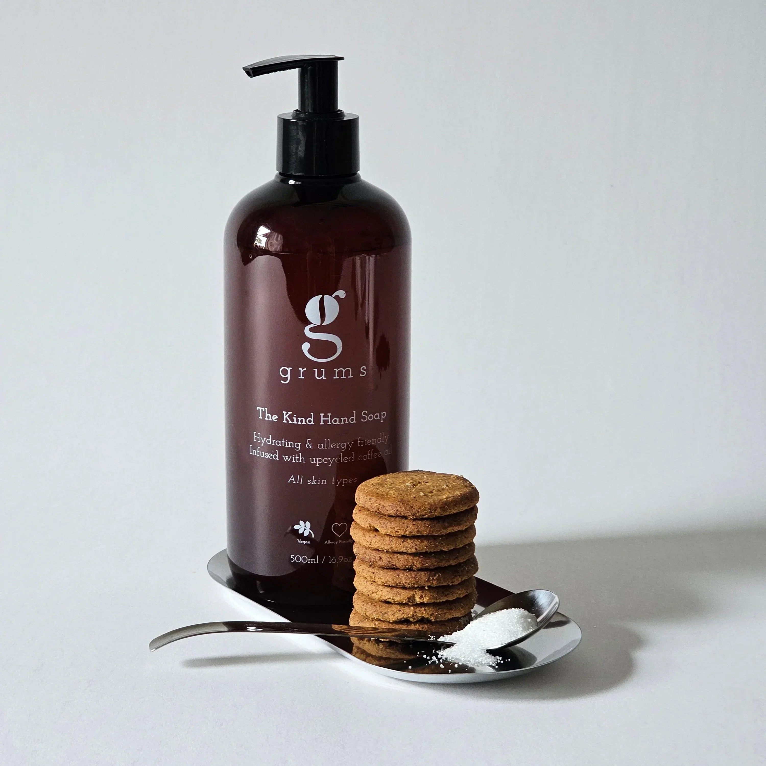 Brown bottle of kind handwash labeled 'grums' with a stack of cookies on a white surface