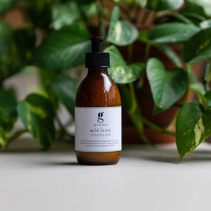 Brown bottle with black cap on a light surface with green plants in the background
