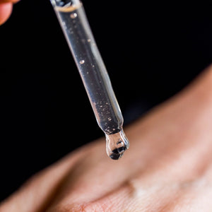 Dropper with a drop of liquid held above skin on a black background