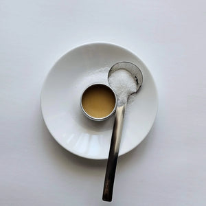White ceramic plate with a small cup and spoon on a light gray background with grums lip balm in the centre