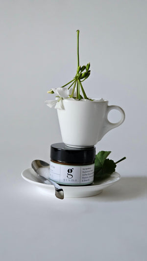 grums hydra calm face cream made from upcycled coffee grounds sitting on a saucer with a espresso cup and white geranium balanced on top