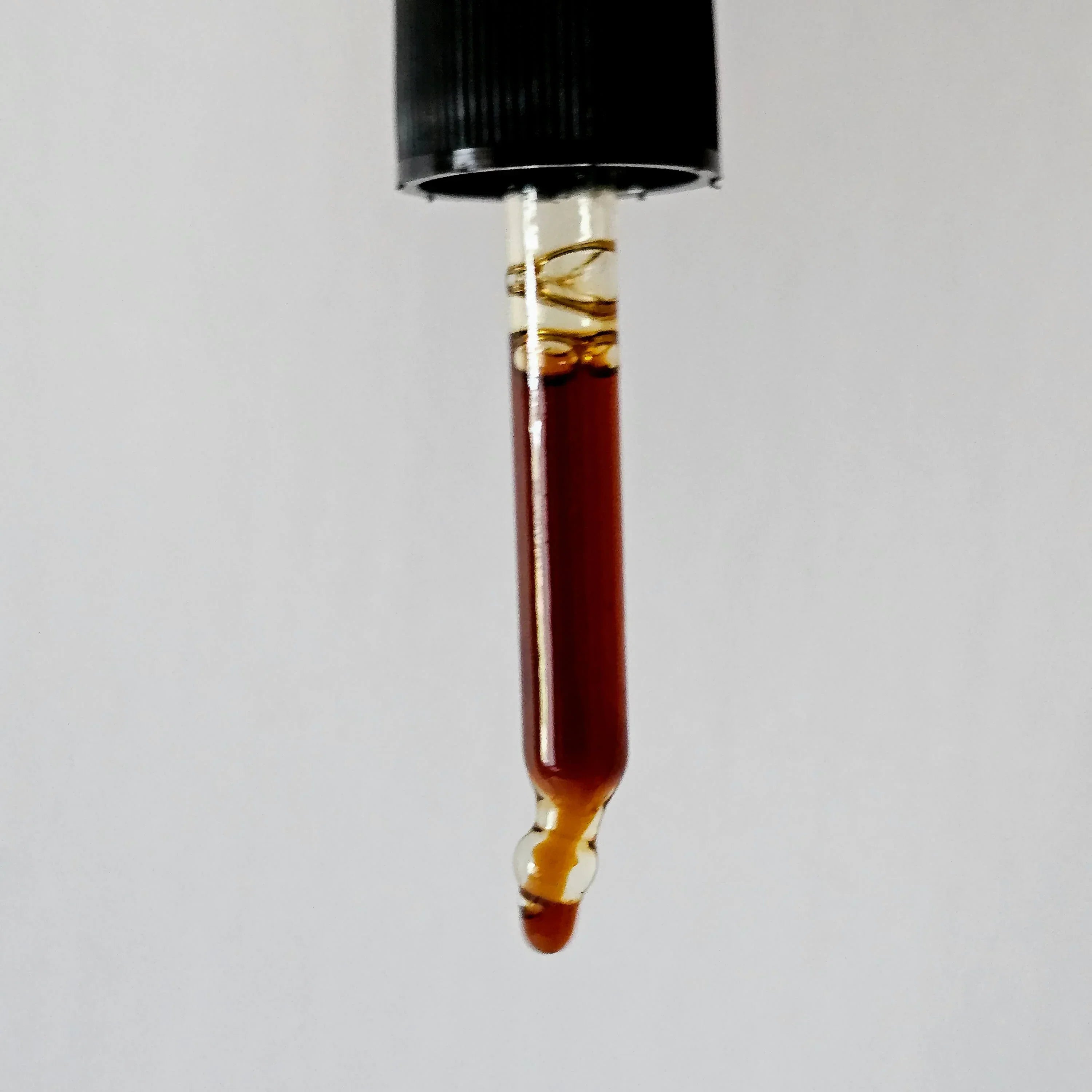 Vial with dark liquid and black cap on a light gray background