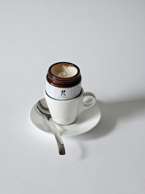 grums hydra calm face cream made from consciously sourced ingredients and upcycled coffee oil. open jar sitting in espresso cup with a spoon to the side.
