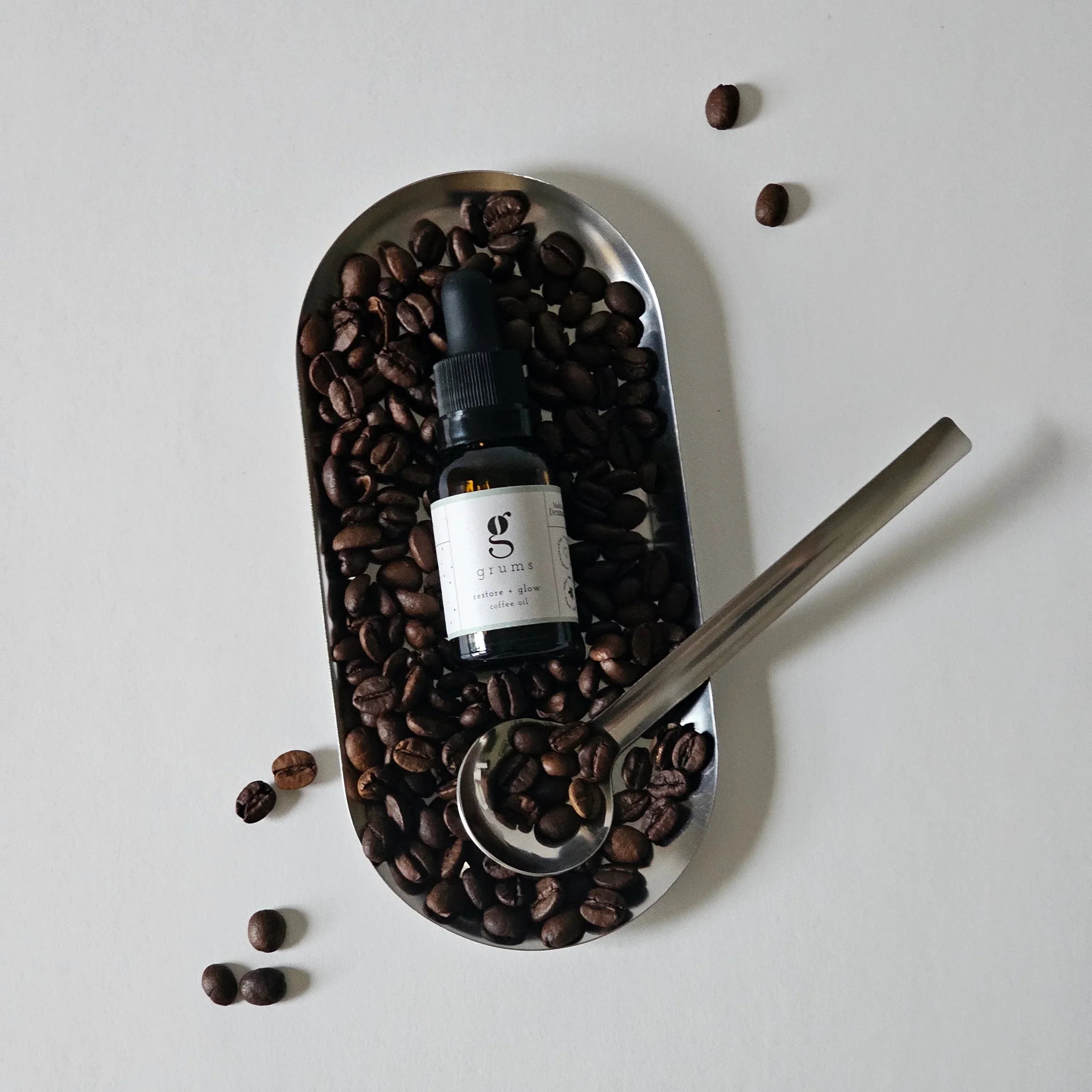 Bottle of coffee extract on a tray with coffee beans and a spoon on a light gray background