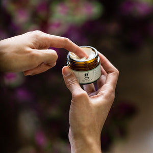 photo showing a hand with finger extended elegantly taking  a small scoop of hydra calm face cream out of a jar