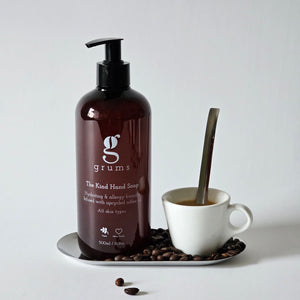 Brown bottle of 'grums' hand soap on a white surface with a cup of coffee and beans.