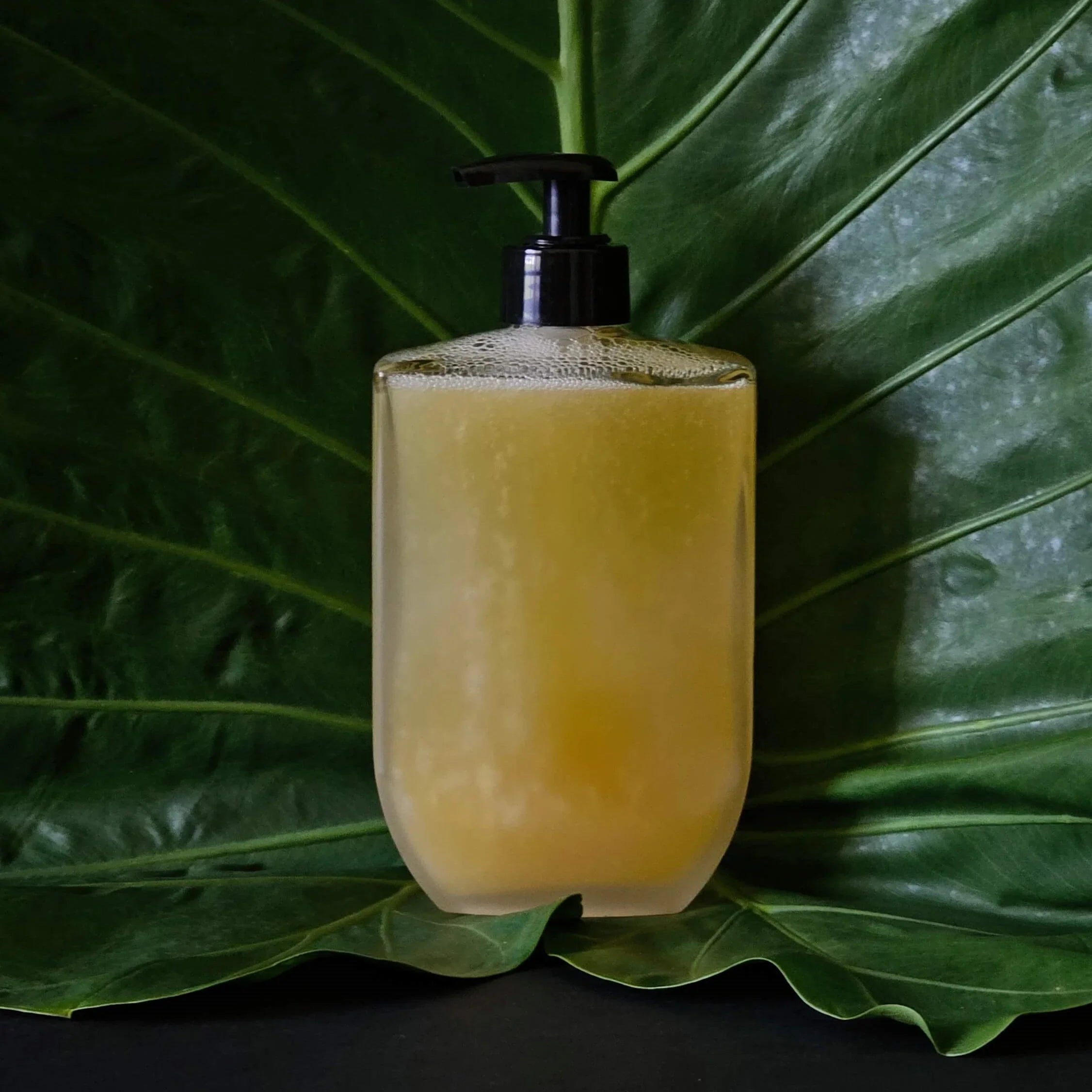 Bottle of yellow mircea liquid soap with pump on a large green leaf